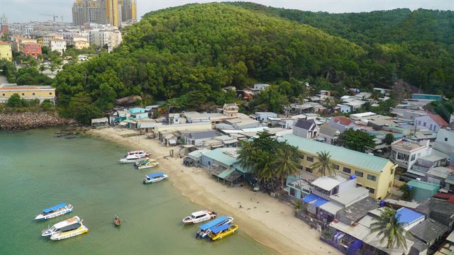 Aerial view of a Phu Quoc fishing village beach with colorful boats and green forested hill
