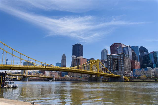Downtown Pittsburgh skyline behind the yellow Roberto Clemente Bridge over the Allegheny River on a sunny day