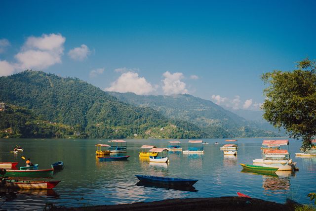 Colorful rowing boats on Phewa Lake in Pokhara below green hills under blue sky