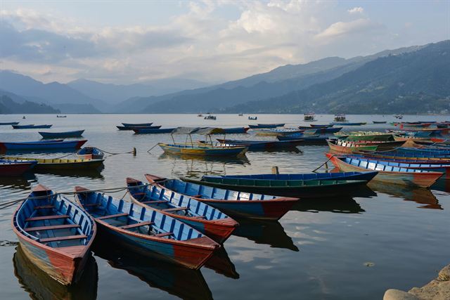 Rows of painted wooden boats moored on Phewa Lake in Pokhara with mountains beyond
