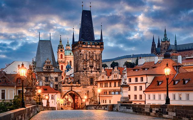 Charles Bridge lamps and Lesser Town Bridge Tower with Prague Castle behind at dusk