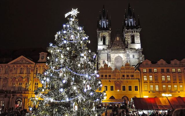 Christmas tree and market in Prague Old Town Square before the lit Tyn Church towers