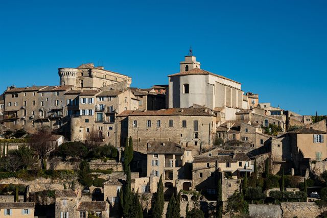 Hilltop village of Gordes in Provence, stone houses stacked below its castle and church under blue sky