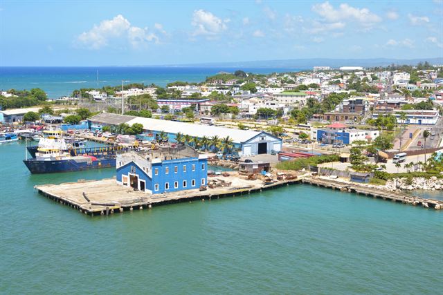Aerial view of Puerto Plata port with a blue warehouse, docked ships and the town beyond