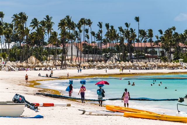Palm-lined Bávaro beach with beach umbrellas, boats and swimmers in Punta Cana, Dominican Republic