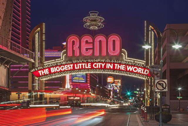 Reno Arch lit in neon at night with traffic streaks on Virginia Street