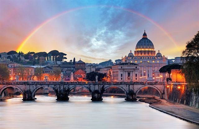 Dome of St. Peter's Basilica behind a Tiber bridge at dusk under a rainbow