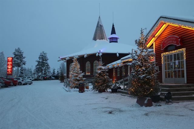 Santa Claus Village in Rovaniemi at snowy twilight with log buildings and Christmas lights