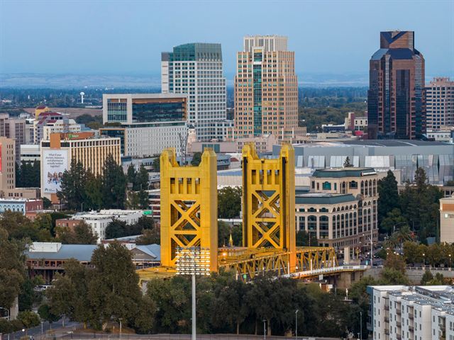 Aerial view of the yellow Tower Bridge in front of the downtown Sacramento skyline and Golden 1 Center area
