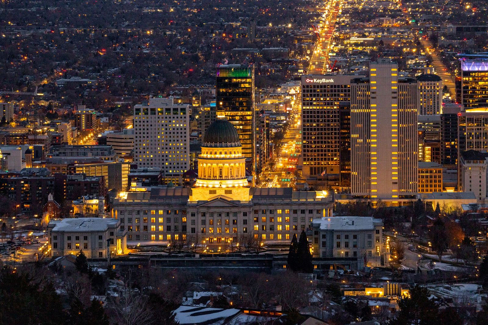 Utah State Capitol dome floodlit at night in front of the glowing downtown Salt Lake City towers