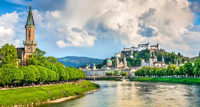 Salzach River riverbank with a church spire and Hohensalzburg Fortress above Salzburg old town