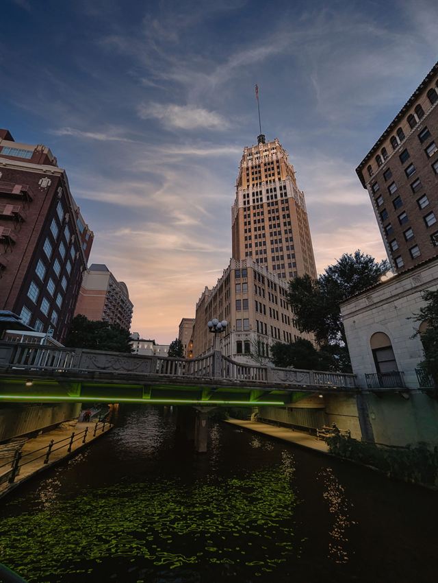 Tower Life Building rising above the San Antonio River Walk under a colorful dusk sky