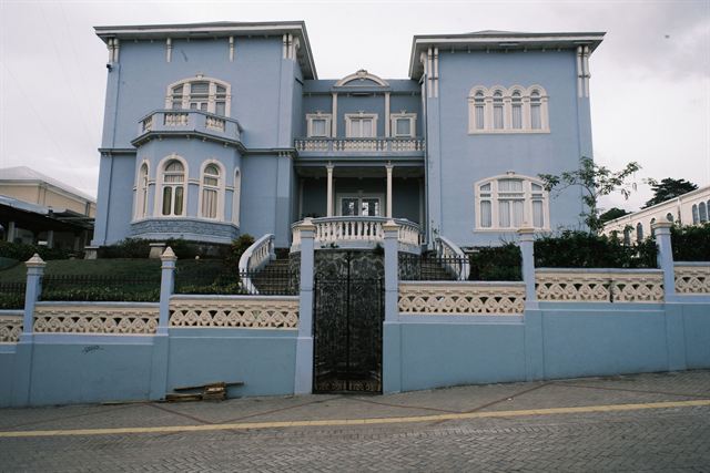 Blue two-story colonial mansion with balconies behind a decorative wall on a street in San Jose, Costa Rica