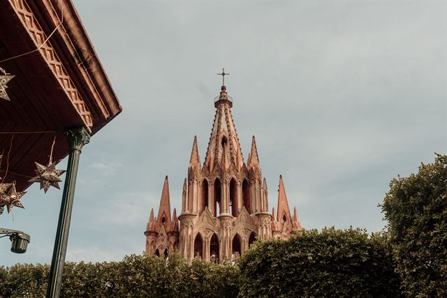 Pink neo-Gothic Parroquia de San Miguel Arcangel towering above trees seen from a colonial street in San Miguel de Allende