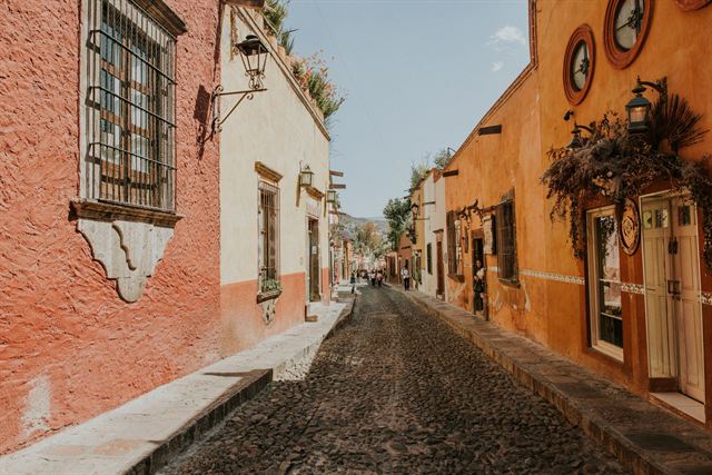 Cobblestone street lined with orange and cream colonial houses with iron balconies in San Miguel de Allende