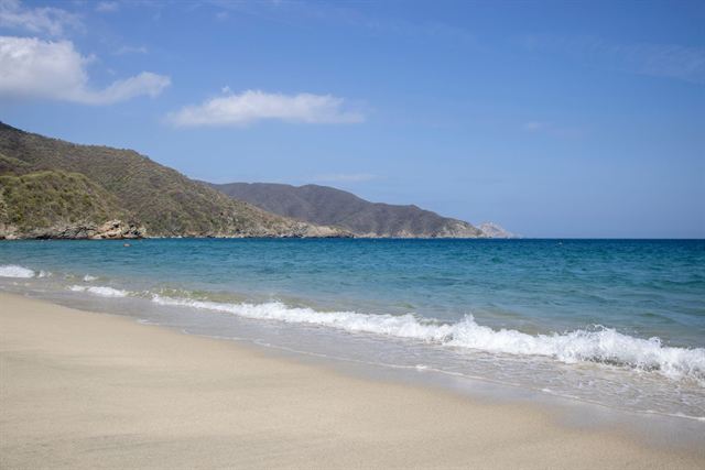 Sandy beach with turquoise surf and green mountains in Tayrona National Park near Santa Marta
