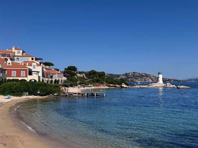 Sandy Sardinian beach with a white lighthouse and terracotta hillside villas on a clear day