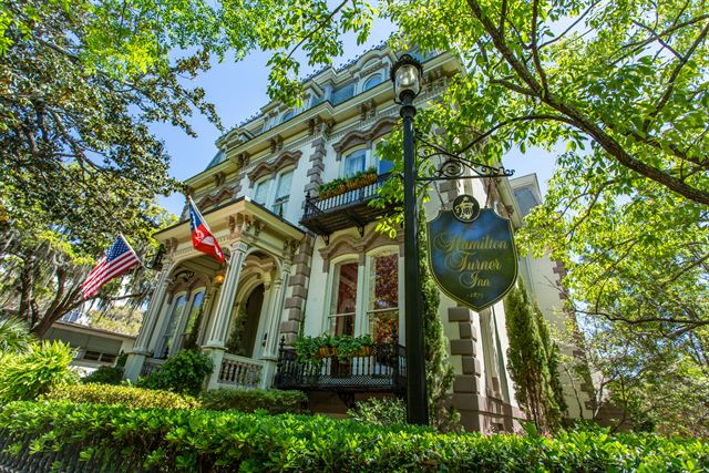 Hamilton-Turner Inn's ornate Victorian mansion and hanging sign under live oaks in Savannah's Lafayette Square