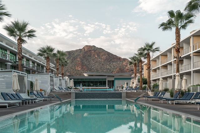 Scottsdale resort swimming pool framed by palm trees and hotel wings with a red desert mountain behind