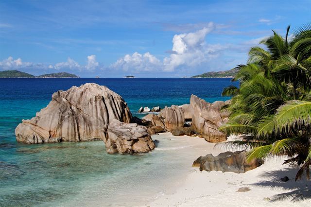 Pink granite boulders, palms and turquoise shallows on a La Digue beach in the Seychelles