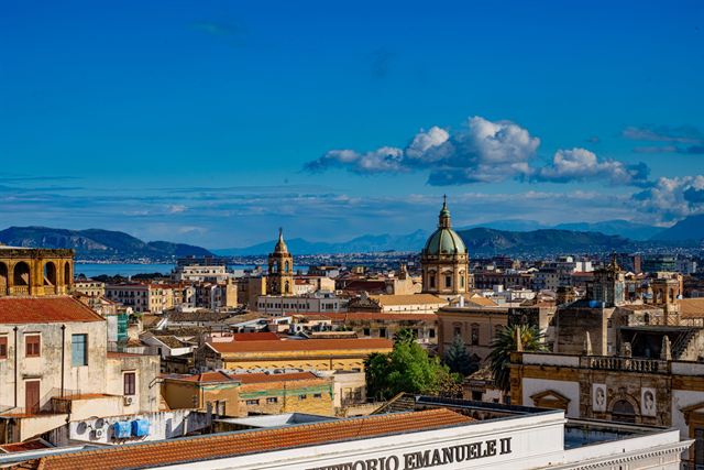 Palermo, Sicily: rooftop skyline with church domes, the bay and mountains under blue sky