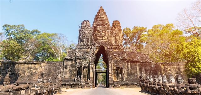 Carved stone face tower gate of Angkor Thom with statues along the causeway