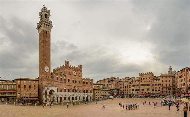 Piazza del Campo in Siena with the Palazzo Pubblico and tall Torre del Mangia under clouds