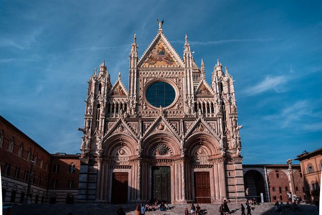 Ornate Gothic facade of Siena Cathedral glowing in sunlight against a deep blue sky