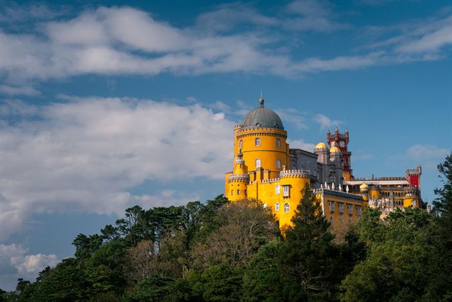Pena Palace in Sintra, yellow and red towers on a wooded hilltop under clouds