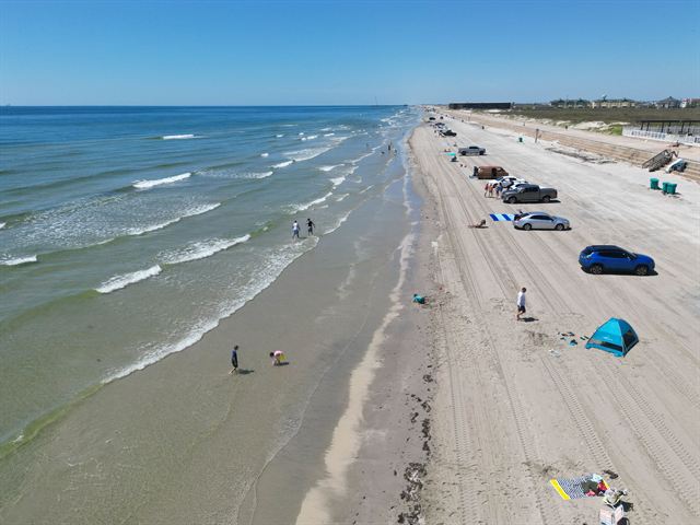 Aerial view of a wide South Padre Island beach with parked cars, tents and waves along the Gulf shoreline