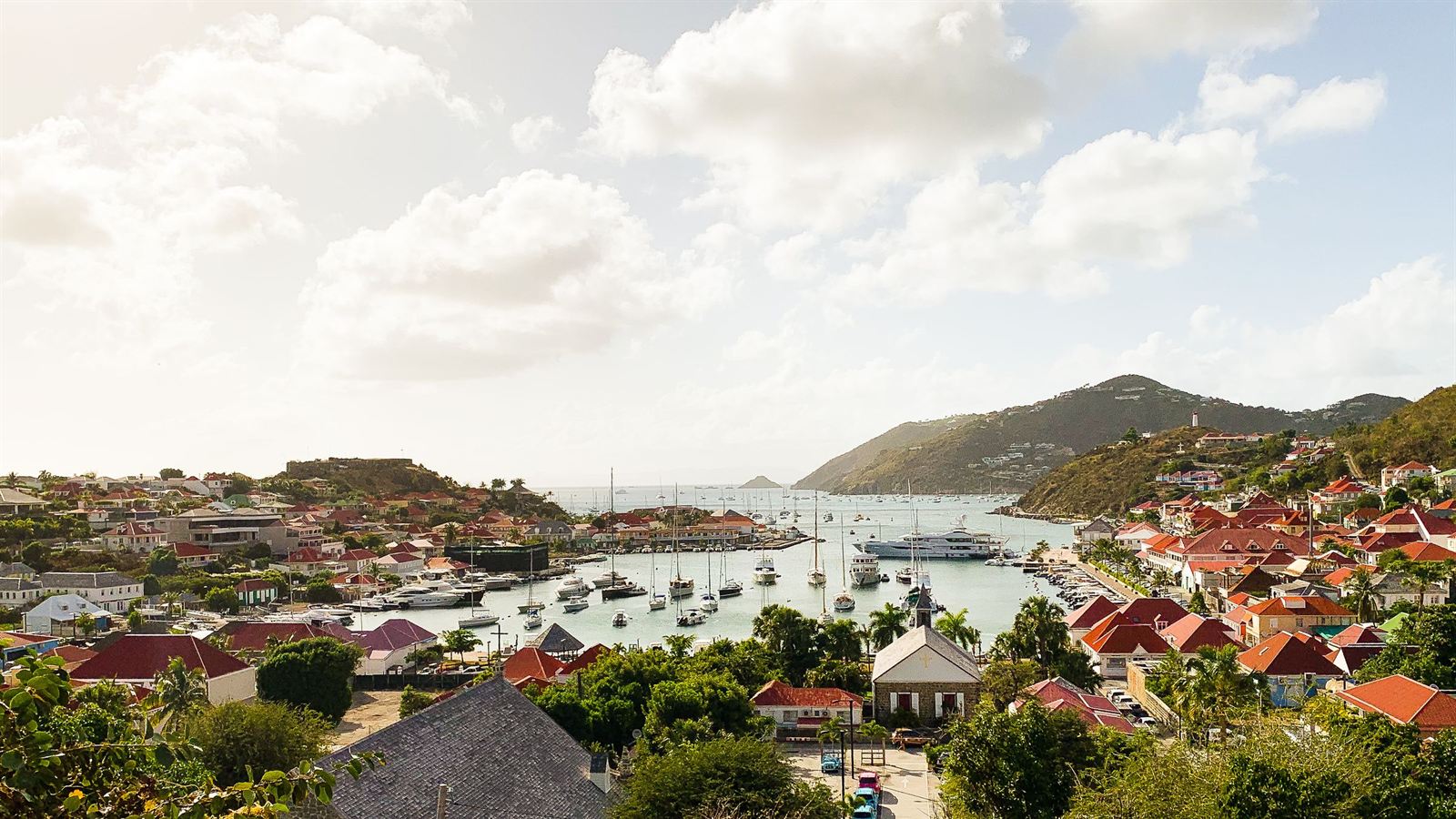 Gustavia harbor on Saint-Barthelemy with red-roofed houses, moored yachts and green hills