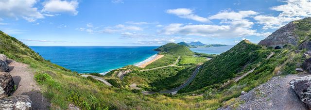 Wide panorama of St Kitts green hills descending to a sandy isthmus and turquoise bays