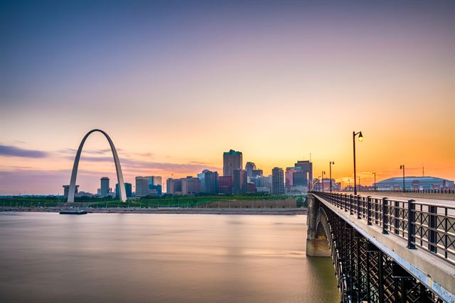 Gateway Arch and St. Louis skyline at sunset seen from a riverside pier across the Mississippi