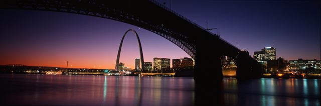 Panorama of the Gateway Arch and St. Louis skyline at dusk framed beneath the Eads Bridge