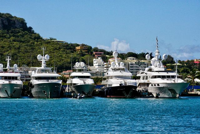 Row of white superyachts moored in a Sint Maarten marina below green hillside homes