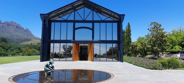 Modern glass-fronted winery building with a reflecting pool and mountain backdrop in Stellenbosch