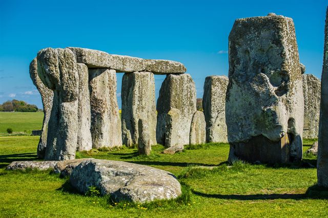Close view of Stonehenge sarsen stones and lintels standing on green grass under blue sky