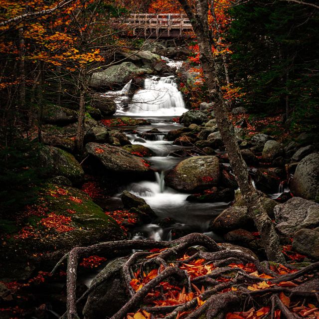 Waterfall cascading over boulders in a Stowe, Vermont forest with red and orange autumn leaves