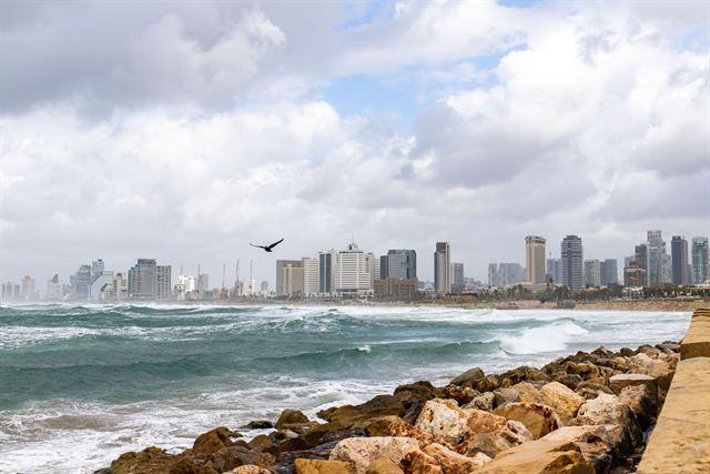 Tel Aviv skyline of high-rise towers seen across waves breaking on a rocky Mediterranean shore