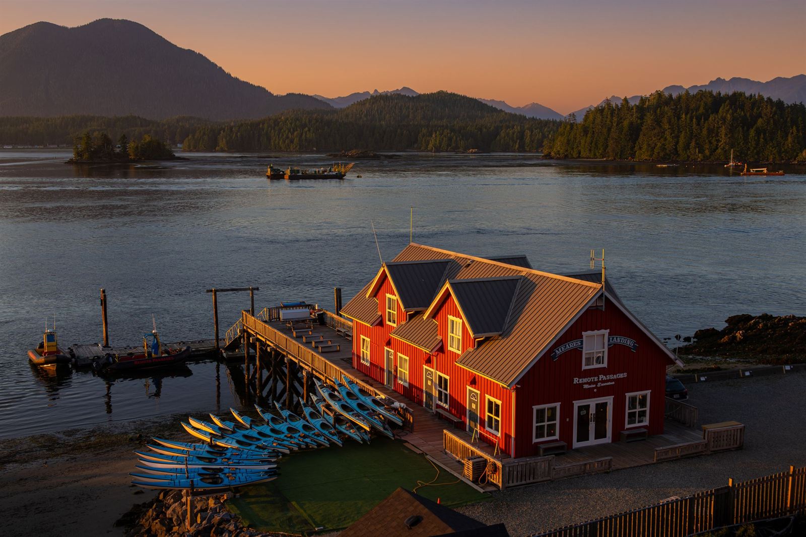 Tofino harbour at sunset with a red waterfront building, kayaks and forested islands and mountains