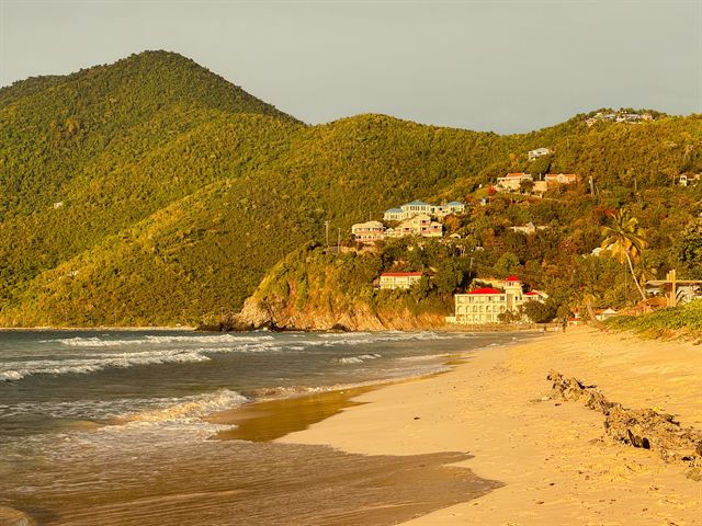 Golden-sand beach backed by steep green hills and hillside villas on Tortola, British Virgin Islands