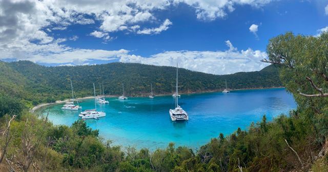 Panoramic view of a sheltered turquoise bay with anchored yachts and forested hills in the British Virgin Islands