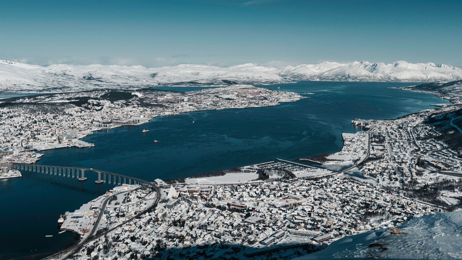 Aerial view of snow-covered Tromso on its island with the Tromso Bridge and Arctic fjord and mountains