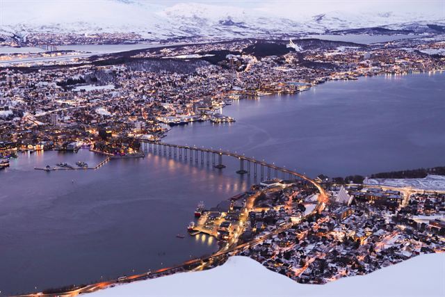 Tromso city lights and bridge across the fjord at winter twilight seen from the mountain above