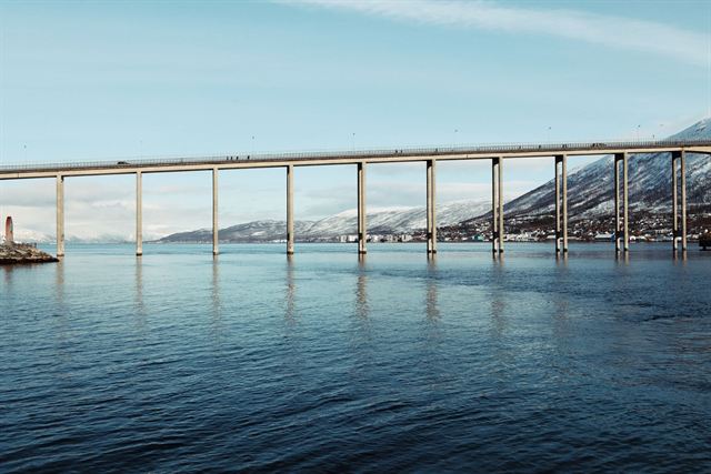 Tromso Bridge spanning calm Arctic water with snowy mountains behind under blue sky