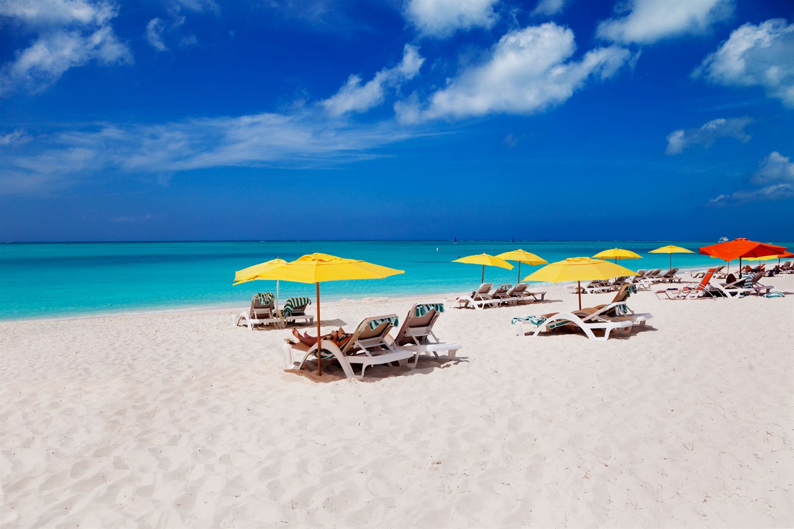 Yellow umbrellas and loungers on the white sand of Grace Bay Beach beside turquoise water, Turks and Caicos
