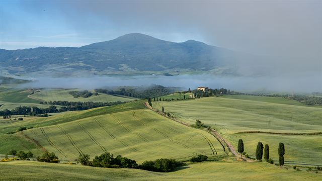 Misty rolling fields near San Quirico d'Orcia in Tuscany with cypress trees and Monte Amiata behind