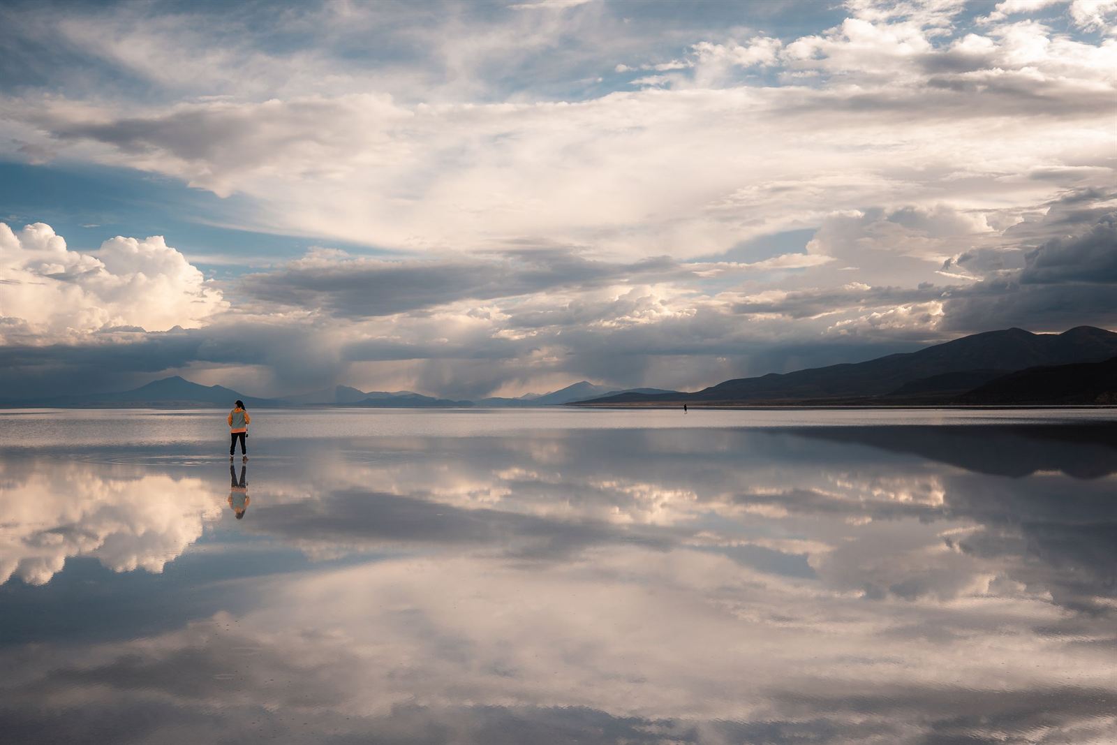 Mirror-like wet salt flat at Salar de Uyuni reflecting clouds and distant mountains with a lone figure