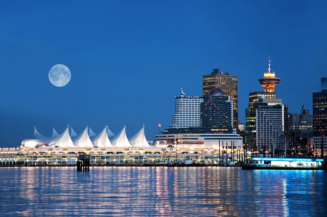 Canada Place's white sails and the downtown Vancouver skyline at night under a full moon