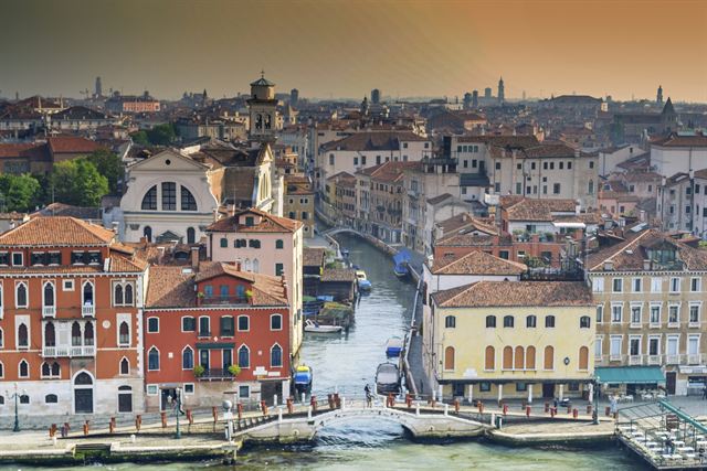 Rooftop view over Venice terracotta roofs, bell towers and a small canal with footbridge